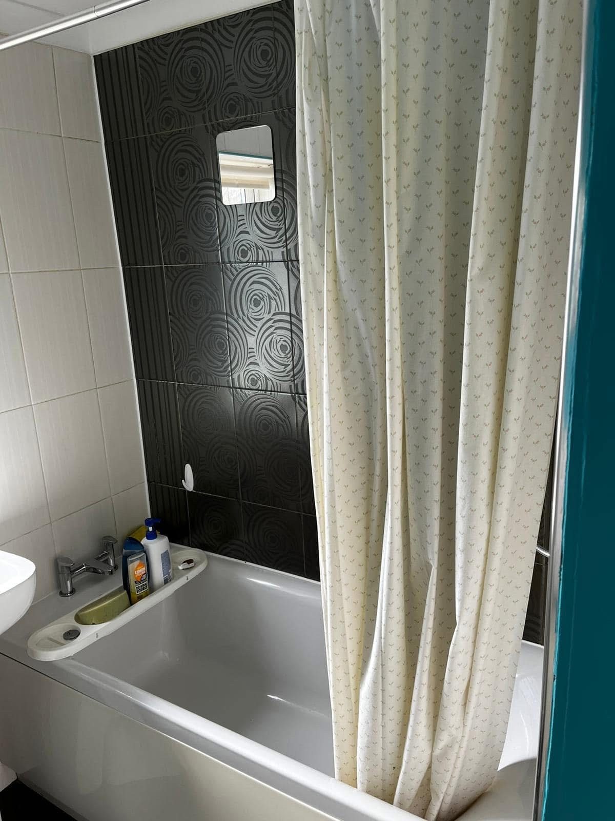 Original bathroom before works, with dated patterned tiles and bath with shower curtain