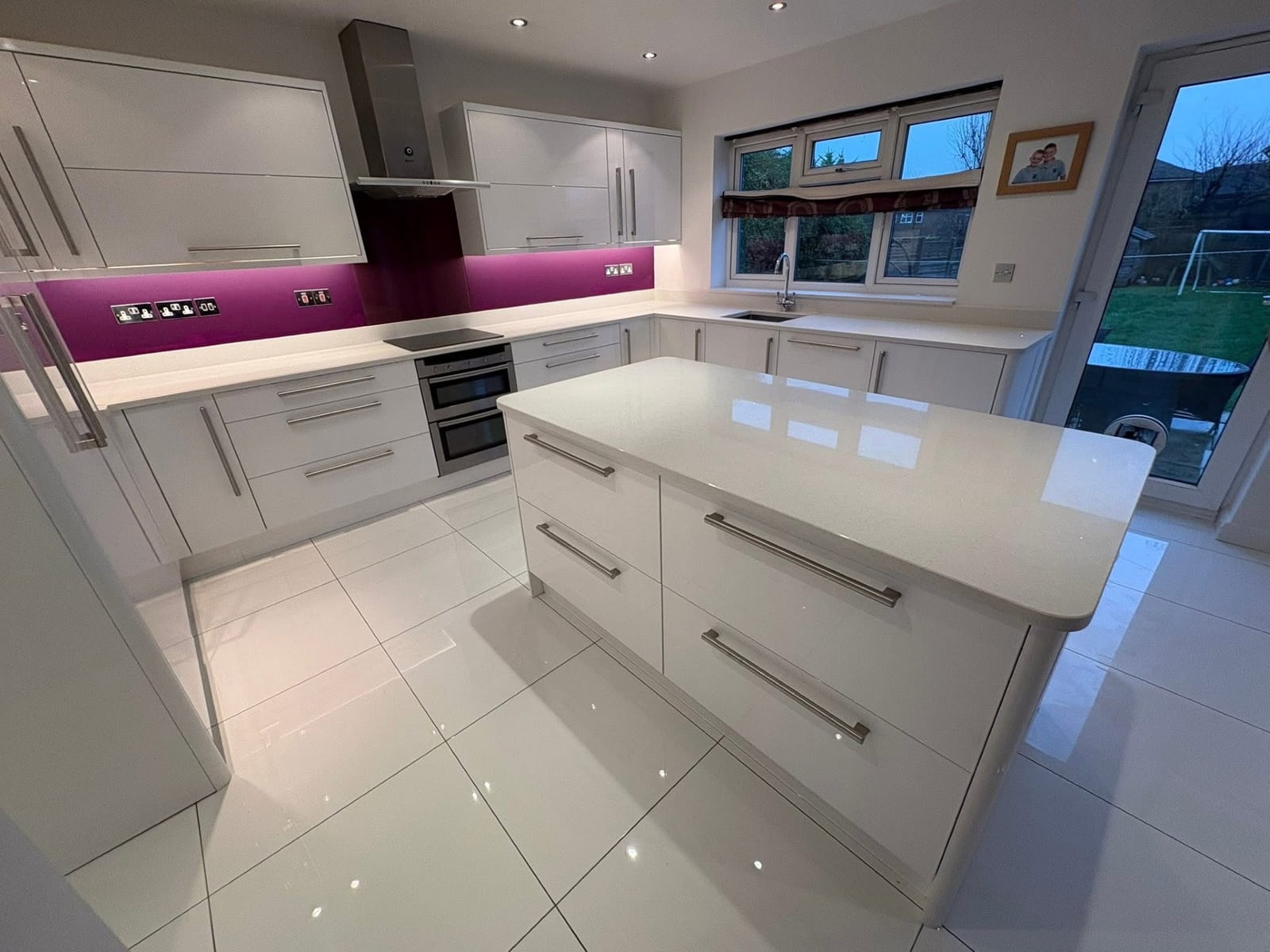 Kitchen island and cooking run finished in white gloss with magenta splashback